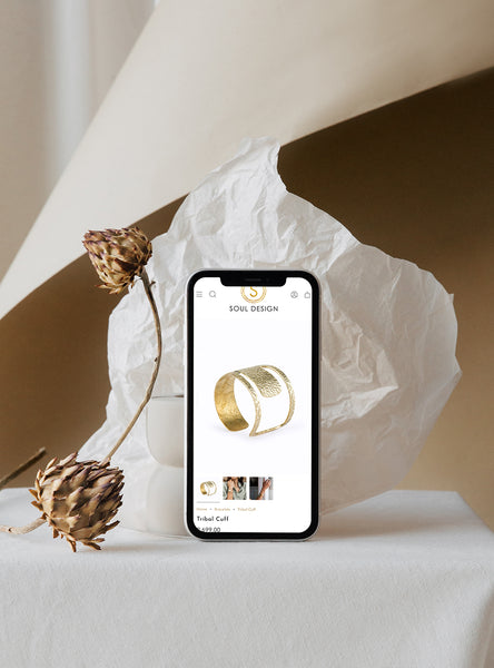Phone displaying a jewelry product page with a gold bracelet on a white surface with decorative elements.